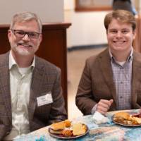 Steven Ferris and other gentleman sitting at table, smiling at camera